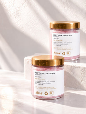 Two jars of ADAY Rosy Crush Salt Scrub on white plinths in sunlight