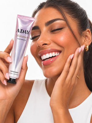 A model smiling while holding the ADAY Pink Shimmer Toothpaste