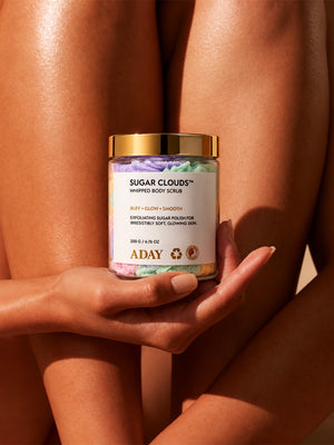 A model holding the ADAY Sugar Clouds Whipped Body Scrub against her legs
