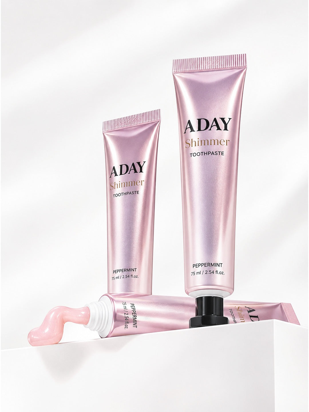 Two tubes of ADAY Pink Shimmer Toothpaste on white plinths, one with a curl of paste