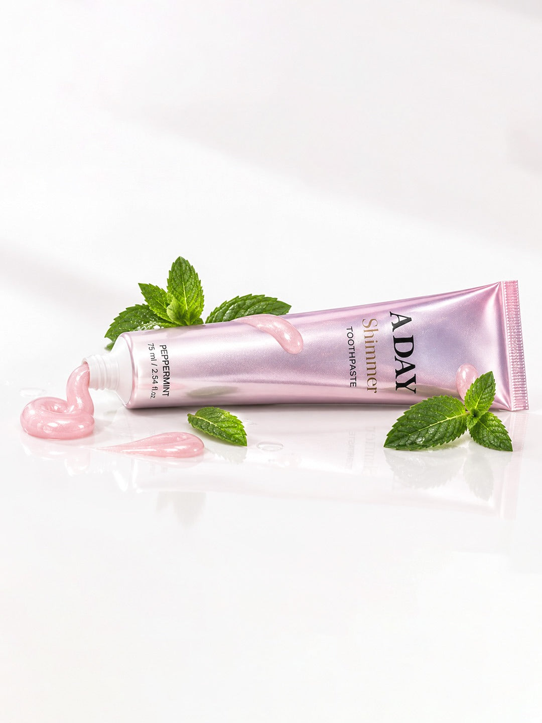 ADAY Pink Shimmer Toothpaste lying with fresh mint leaves and a curl of pink paste