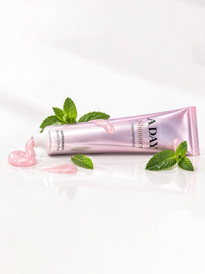 ADAY Pink Shimmer Toothpaste lying with fresh mint leaves and a curl of pink paste
