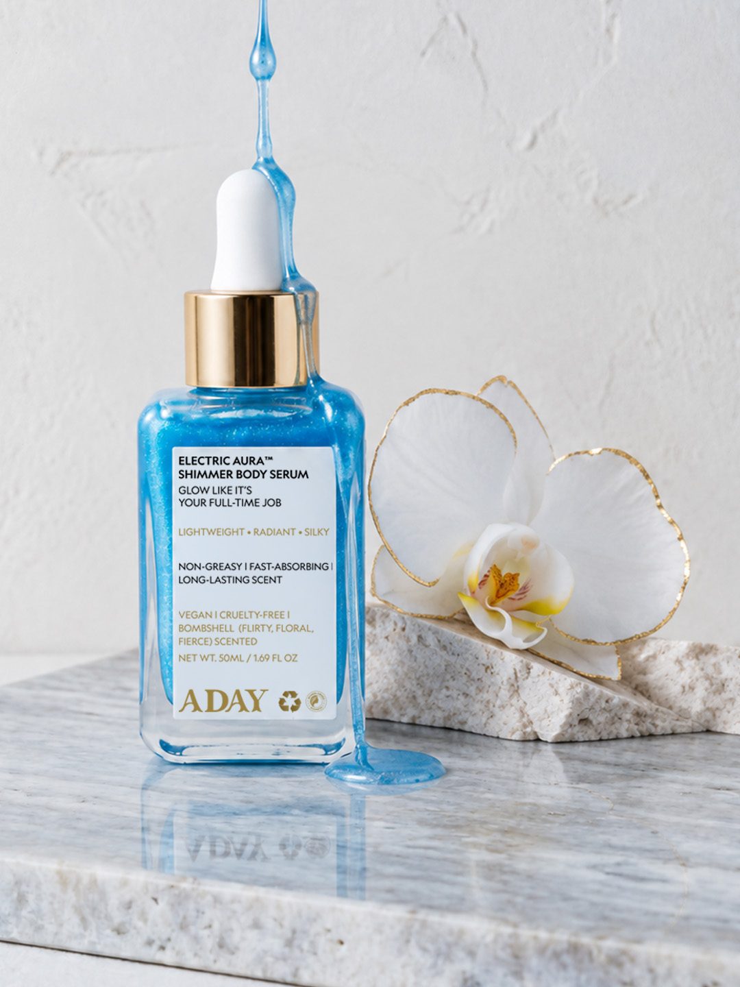 Electric Aura Shimmer Body Serum beside an orchid on marble