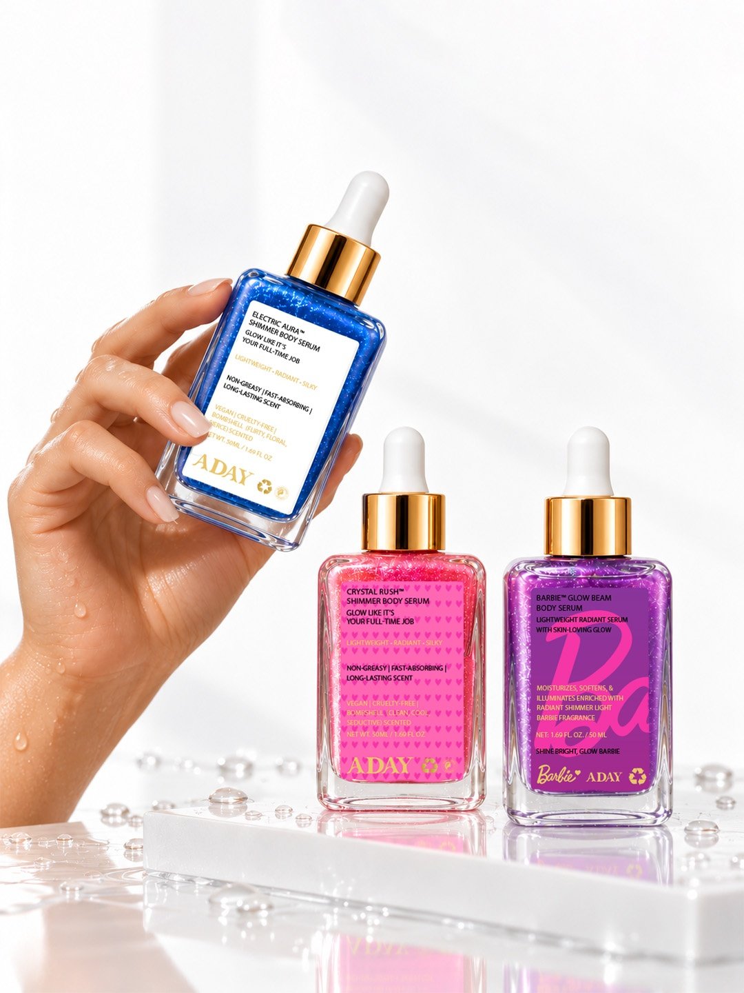A hand holding the ADAY Electric Aura body serum, with the Crystal Rush and ADAY x Barbie serums alongside